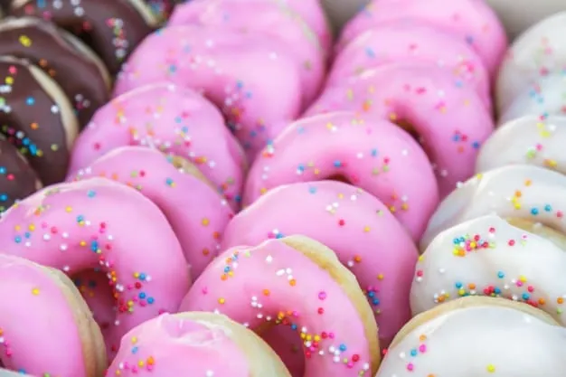 Primer plano de una bandeja con donas glaseadas de fresa, chocolate y vainilla con chispas de colores, representando la disponibilidad y tentación de los alimentos ultraprocesados.