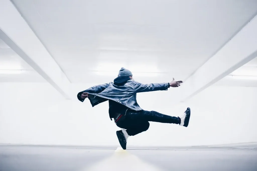 Hombre realizando un salto de baile urbano o parkour en un espacio minimalista blanco que representa el movimiento y la salud