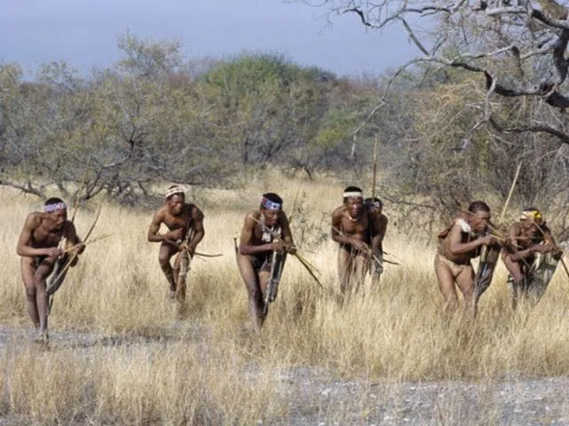 Grupo de hombres de una tribu de cazadores-recolectores corriendo por la sabana con arcos y flechas, representando el movimiento humano natural.