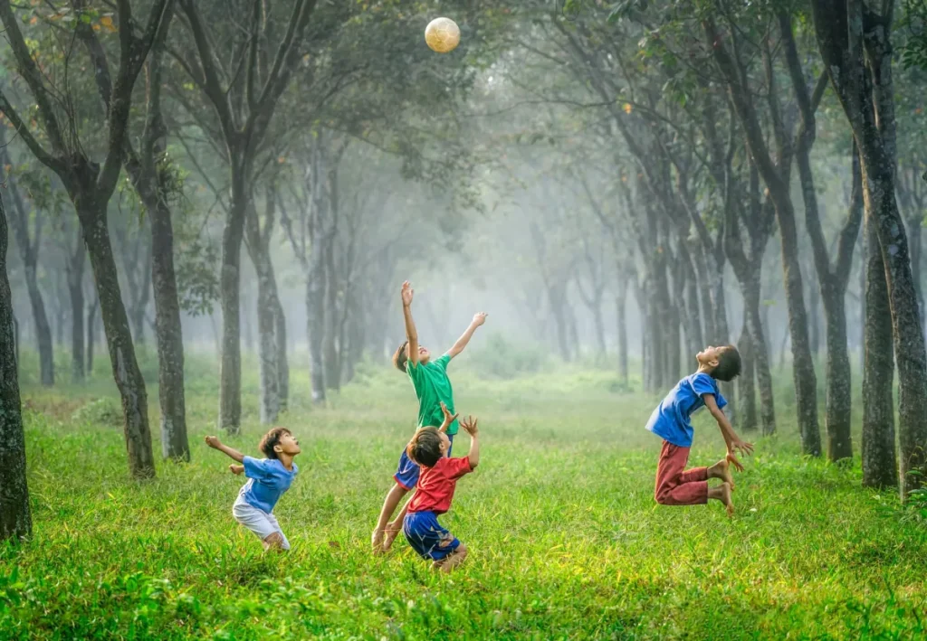 Grupo de niños jugando con una pelota en un entorno boscoso, representando la importancia del movimiento natural para la salud