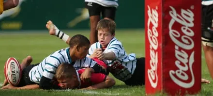 Niños jugando un partido de rugby junto a una valla publicitaria de Coca-Cola
