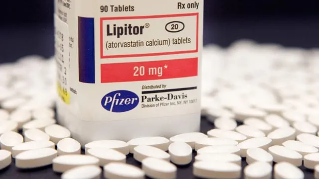 Frasco de Lipitor (atorvastatina) de 20 mg rodeado de pastillas blancas sobre una superficie oscura.