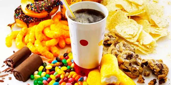Bodegón de alimentos ultraprocesados que incluye refrescos azucarados, donuts, patatas fritas, galletas y golosinas, ilustrando el impacto del azúcar y los procesados en la salud.