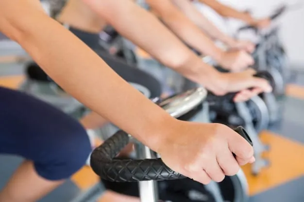 Beneficios del entrenamiento de ciclo indoor y spinning Primer plano de manos de personas entrenando en bicicletas de spinning en un gimnasio