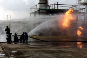 Equipo de bomberos extinguiendo un incendio industrial con mangueras de agua, utilizado como metáfora visual sobre la importancia de la prevención del infarto de corazón.