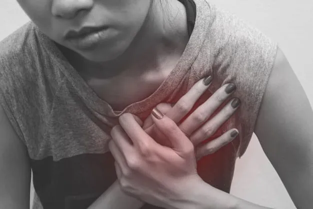 Primer plano en blanco y negro de una persona presionando su pecho con la mano, expresando dolor o síntoma de infarto.