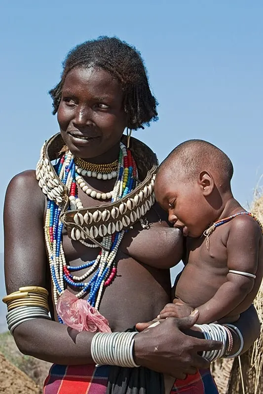 Mujer de una tribu indígena amamantando a su bebé, representando la lactancia materna natural en un contexto evolutivo.