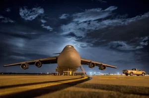 Avión de carga de grandes dimensiones estacionado en la pista de un aeropuerto durante la noche, con un vehículo de apoyo al lado.